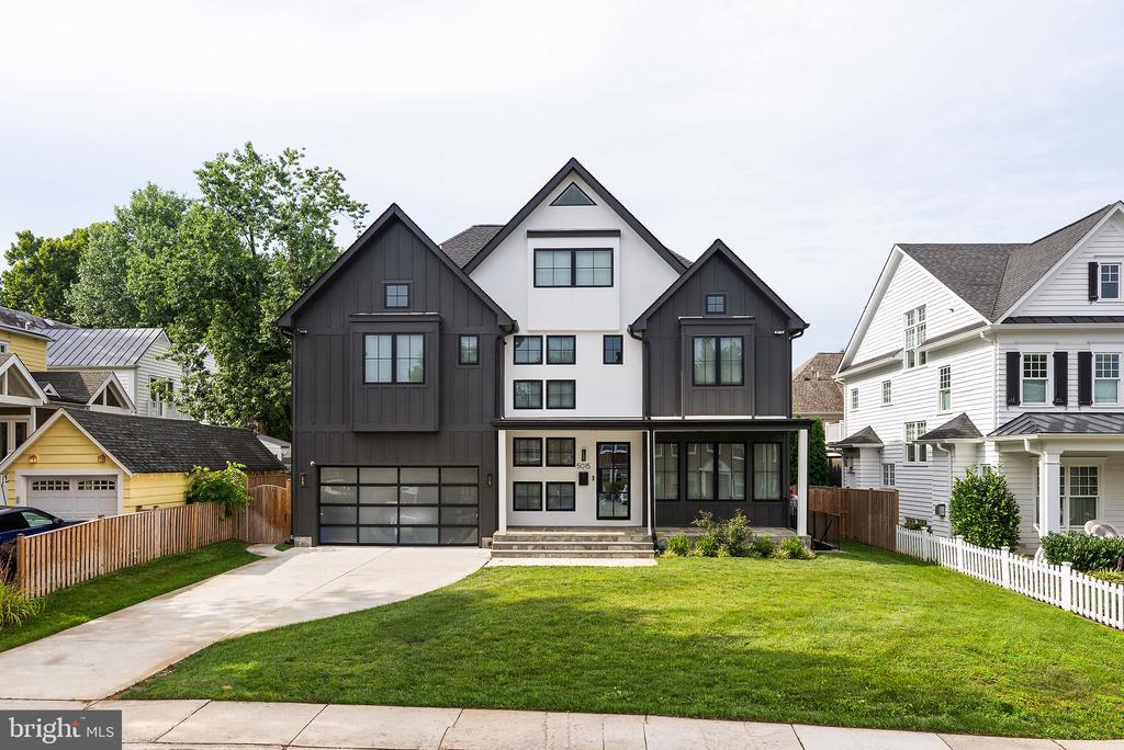 Modern charcoal-and-white home with steep gables, a glass-paneled garage door, and a broad front lawn.
