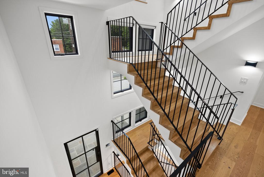 Bright stairwell with wood stairs, black metal railings, and tall windows.