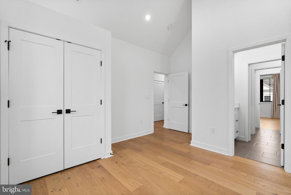 Unfurnished interior with white double doors, light hardwood floors, and adjoining doorways.