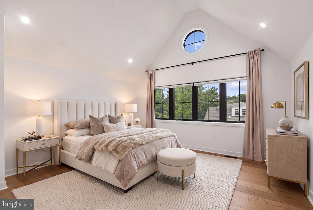 Bedroom with a vaulted ceiling, circular window, and large black-framed window overlooking trees.