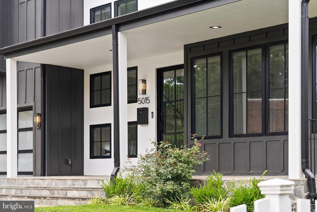 Contemporary home entrance with charcoal siding, white porch columns, black-framed windows, and stone steps.