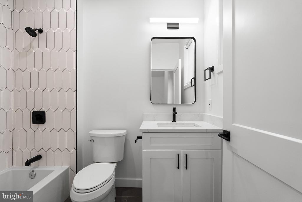 Bathroom with a white vanity, black fixtures, geometric shower tile, toilet, and bathtub.