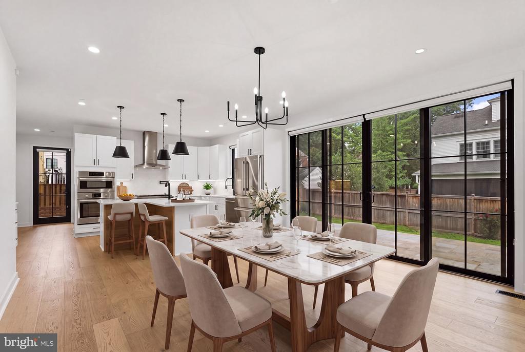 Open kitchen and dining area with white cabinets, a large table, and black-framed backyard doors.