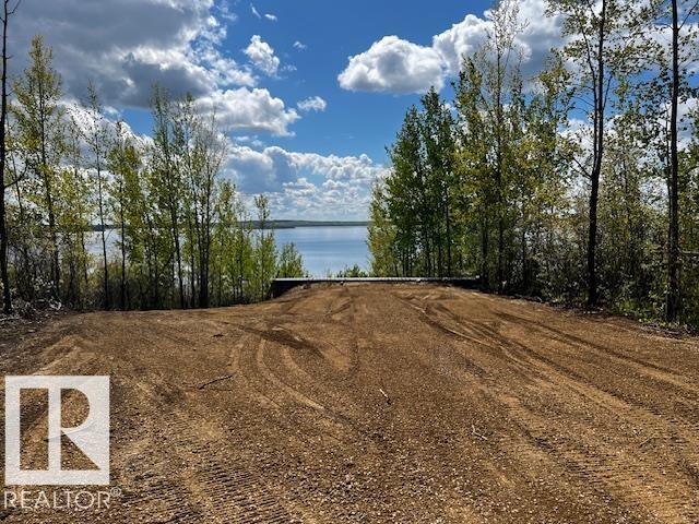 Cleared lakeside lot with a broad dirt area and a view of the water through trees.