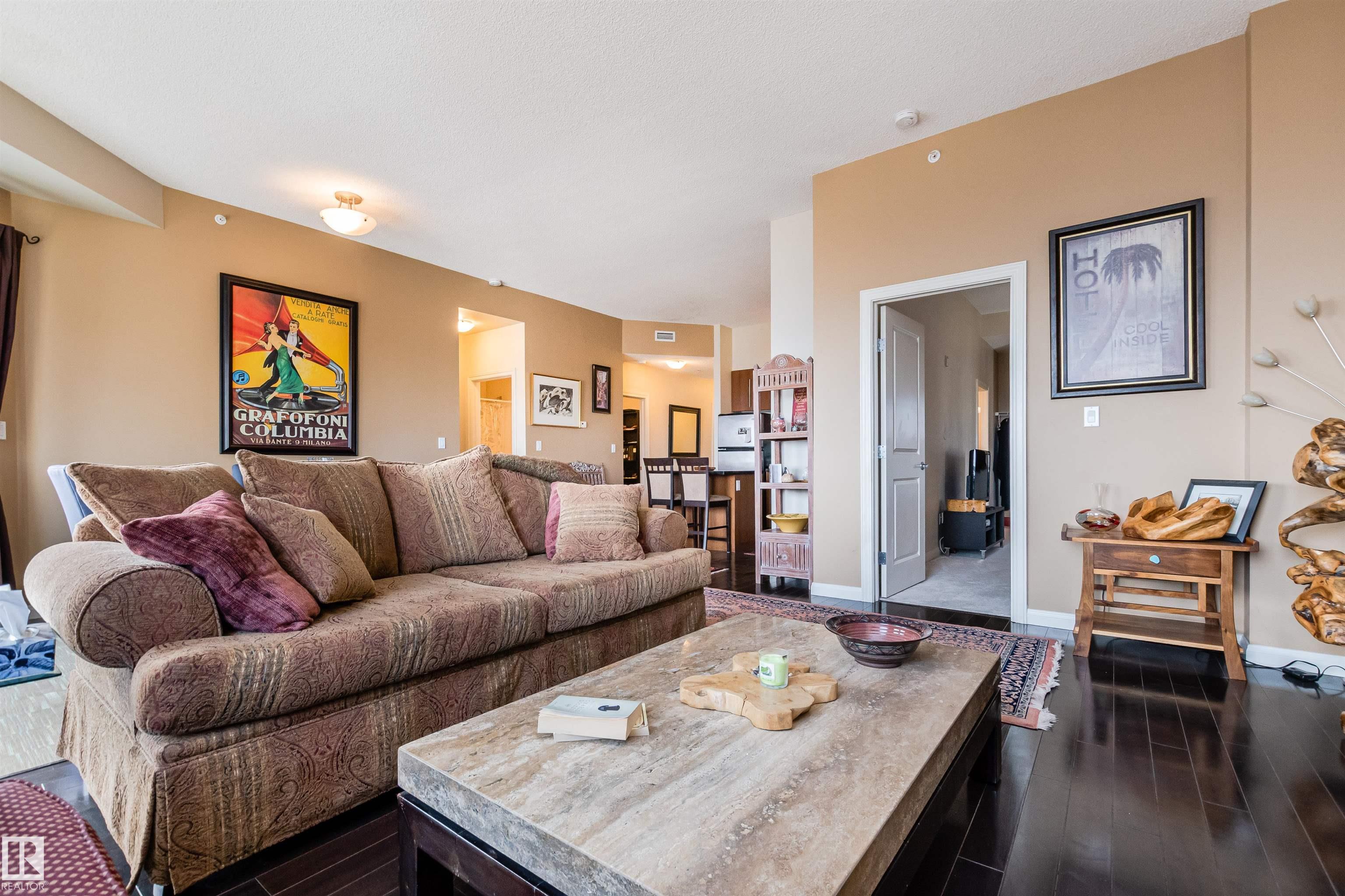 Furnished condo living room with a patterned sectional, stone coffee table, and dark wood floors.