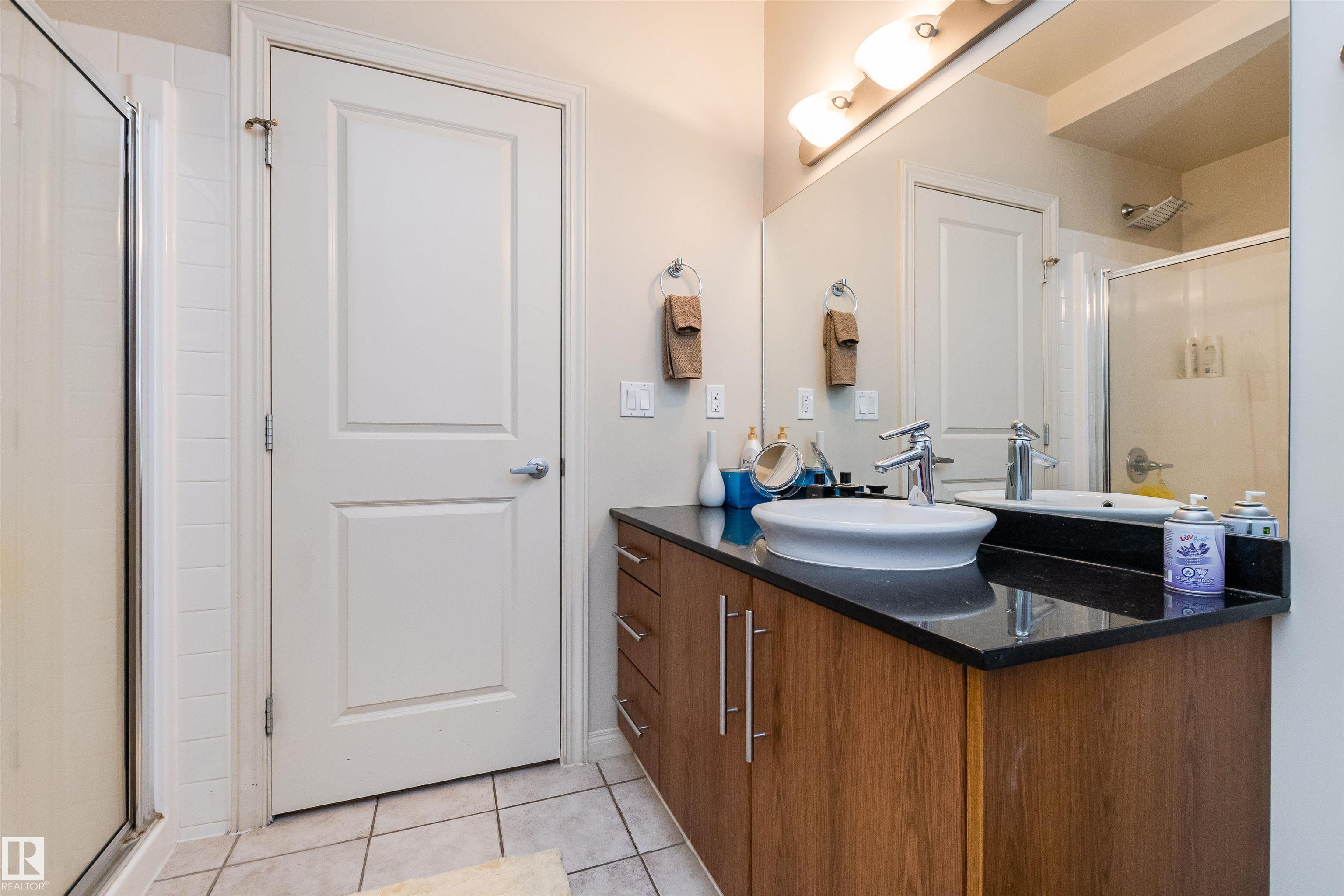 Bathroom with a wood vanity, black countertop, vessel sink, and glass-enclosed shower.