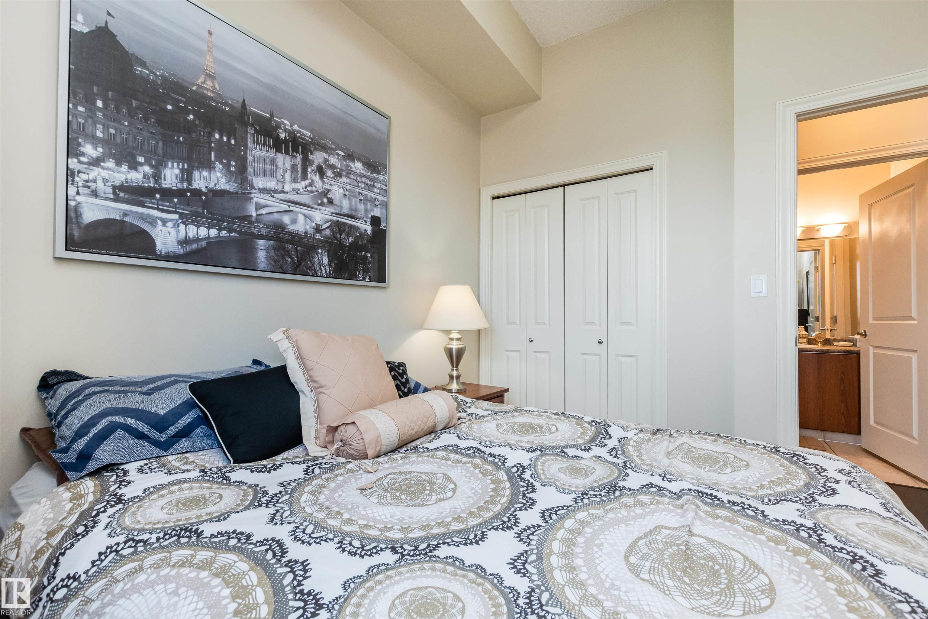 Furnished bedroom with patterned bedding, a Paris cityscape print, and an open doorway to the bathroom.