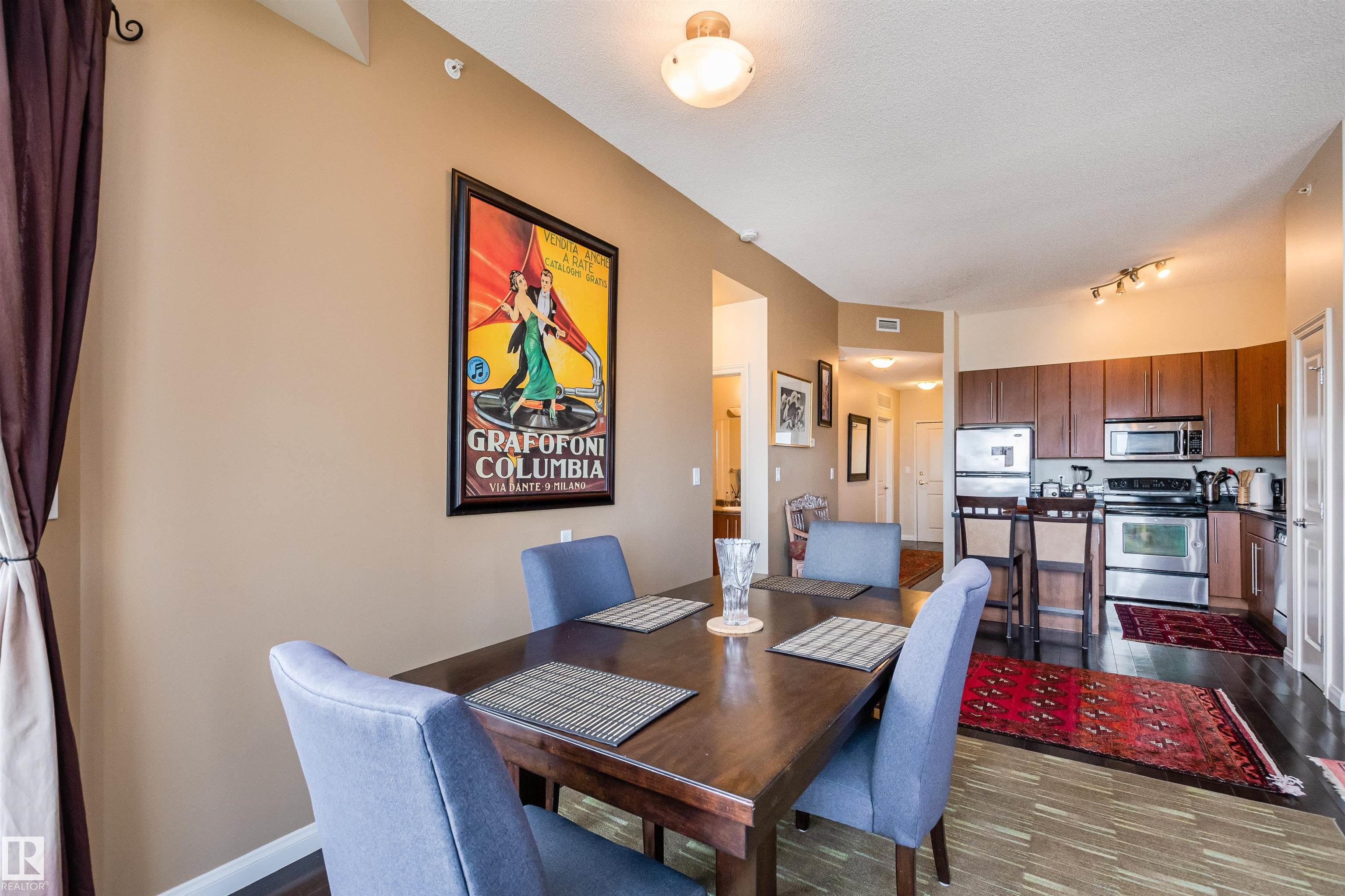 Dining area with blue chairs and a dark wood table opening into a kitchen with stainless steel appliances.