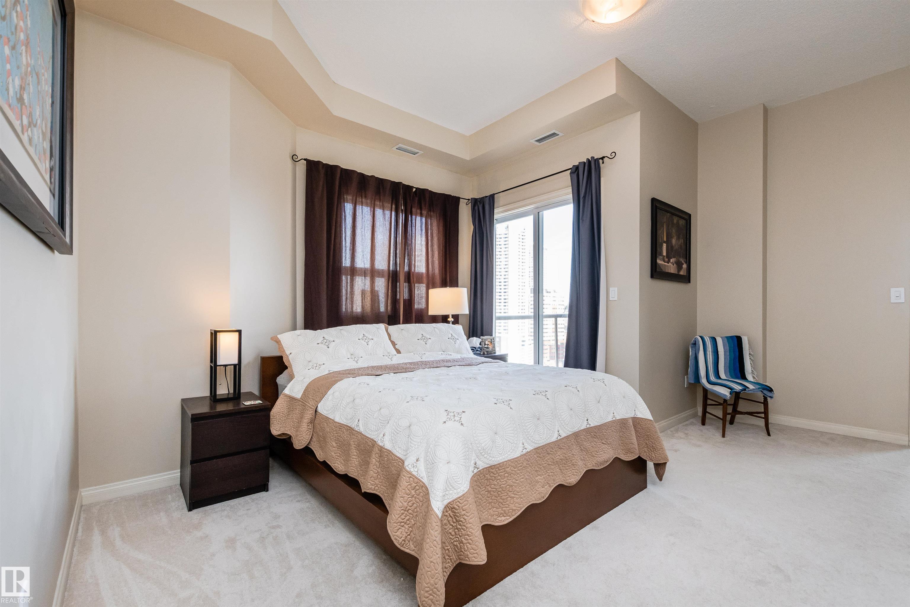 Bedroom with a large patterned bed and a window overlooking high-rise buildings.