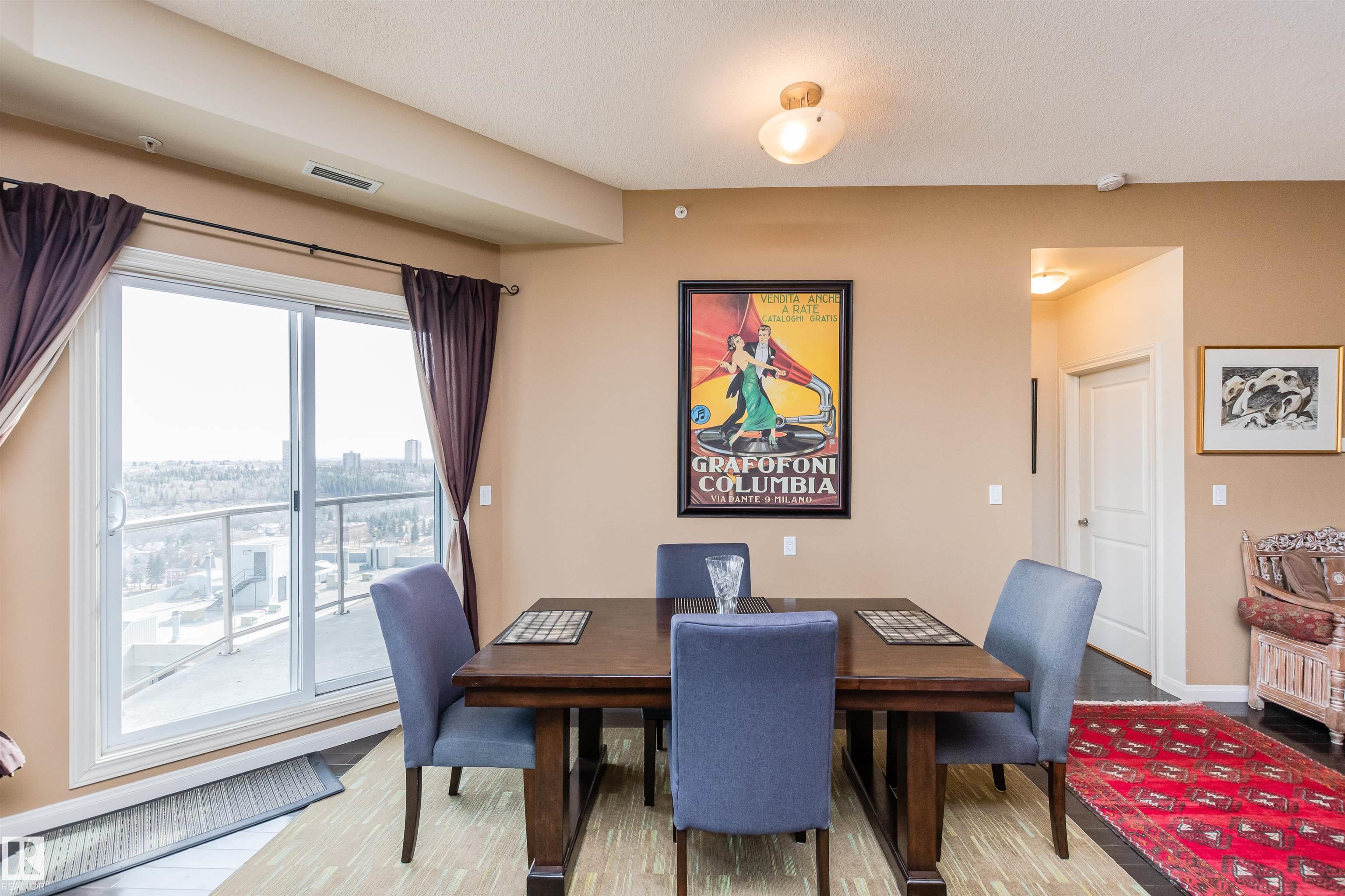 Furnished dining room with blue chairs, a vintage Columbia poster, and sliding doors to a balcony.