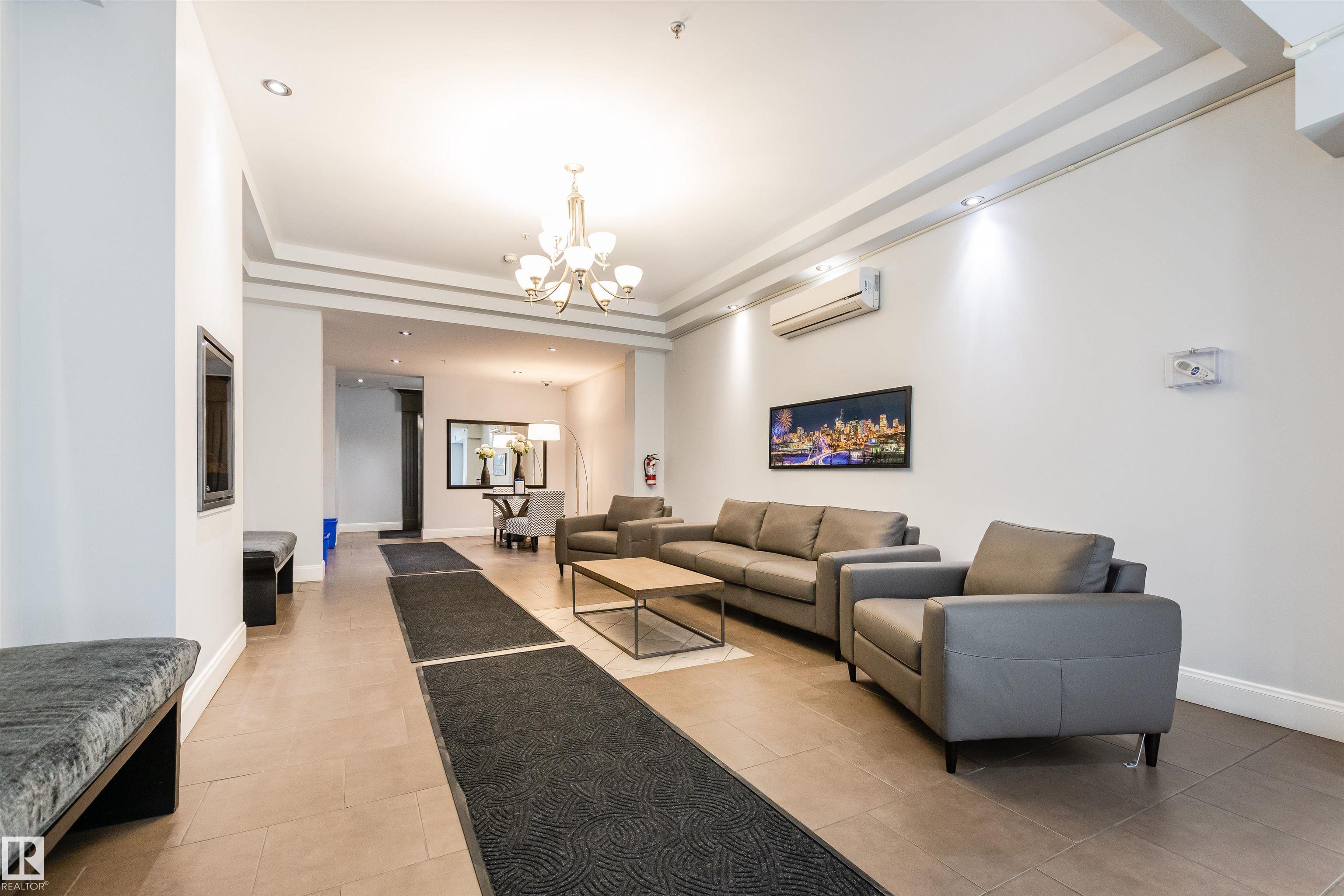 Condominium lobby lounge with gray seating, dark floor runners, a chandelier, and framed city artwork.