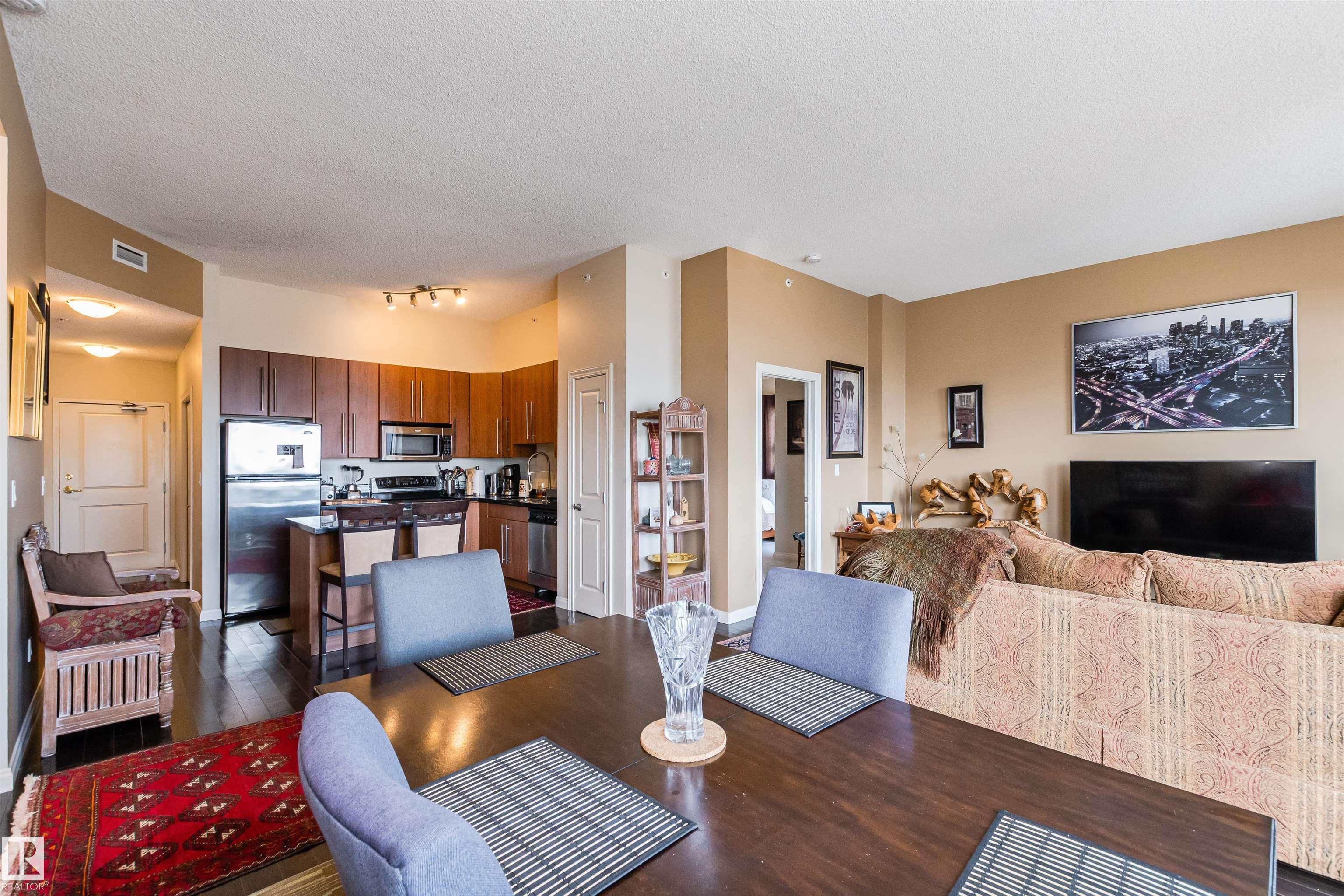 Open-plan condo living and dining area with a patterned sofa and kitchen with stainless steel appliances.