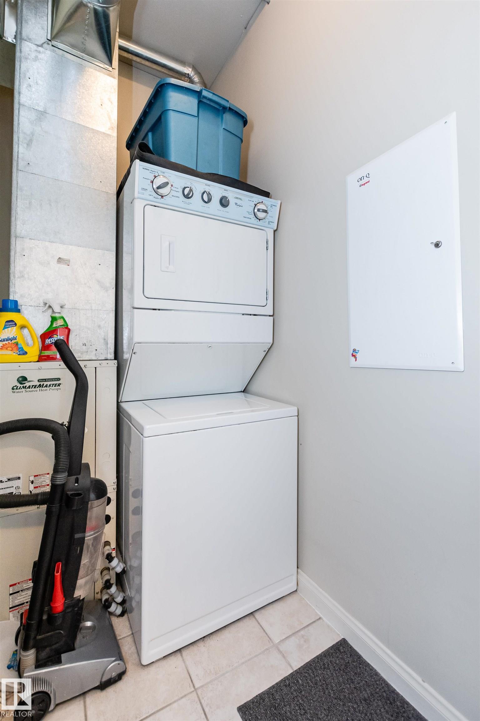Laundry room with stacked washer and dryer beside a heat pump and vacuum cleaner.