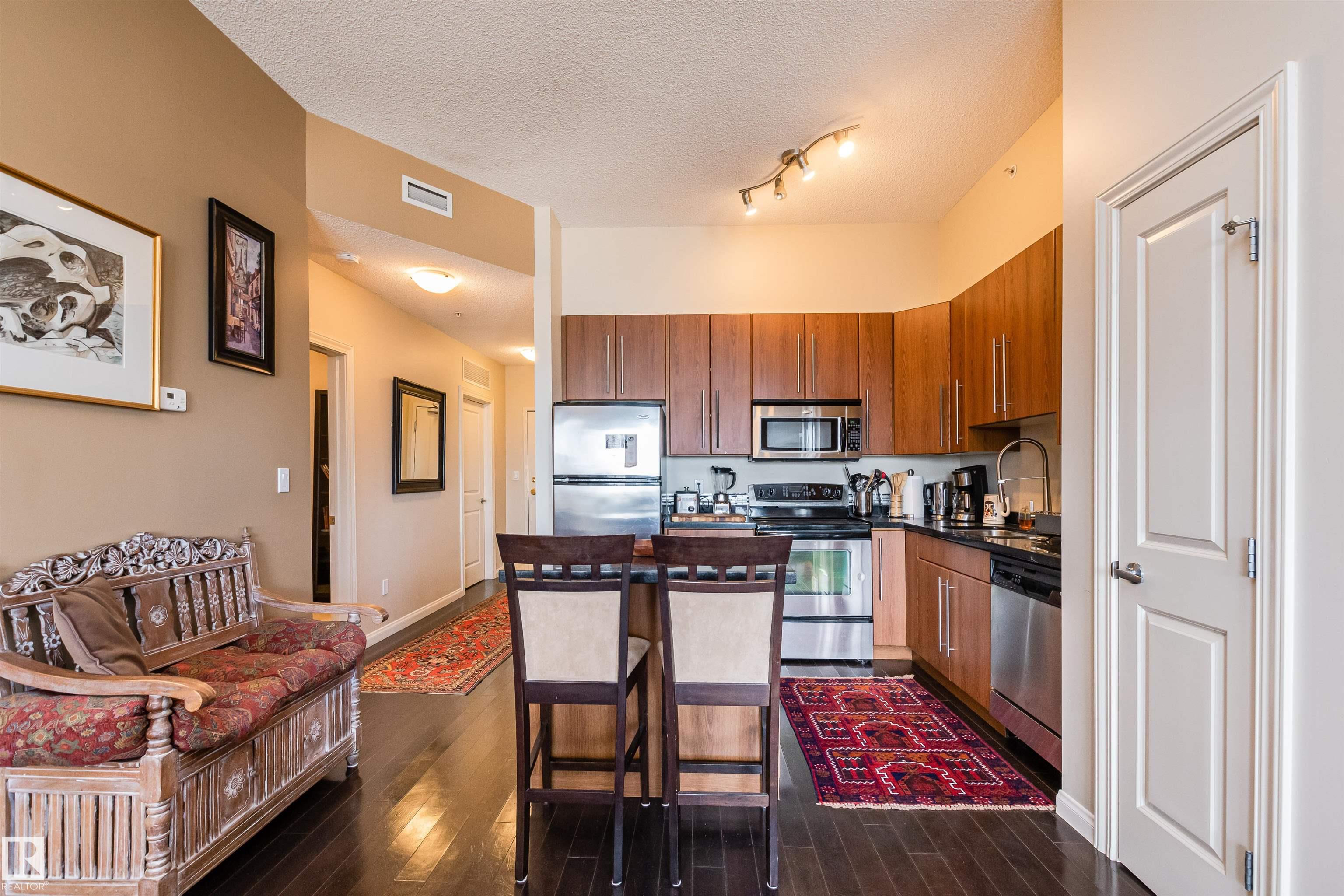 Condo kitchen with wood cabinets, stainless steel appliances, breakfast bar, and carved wooden settee.