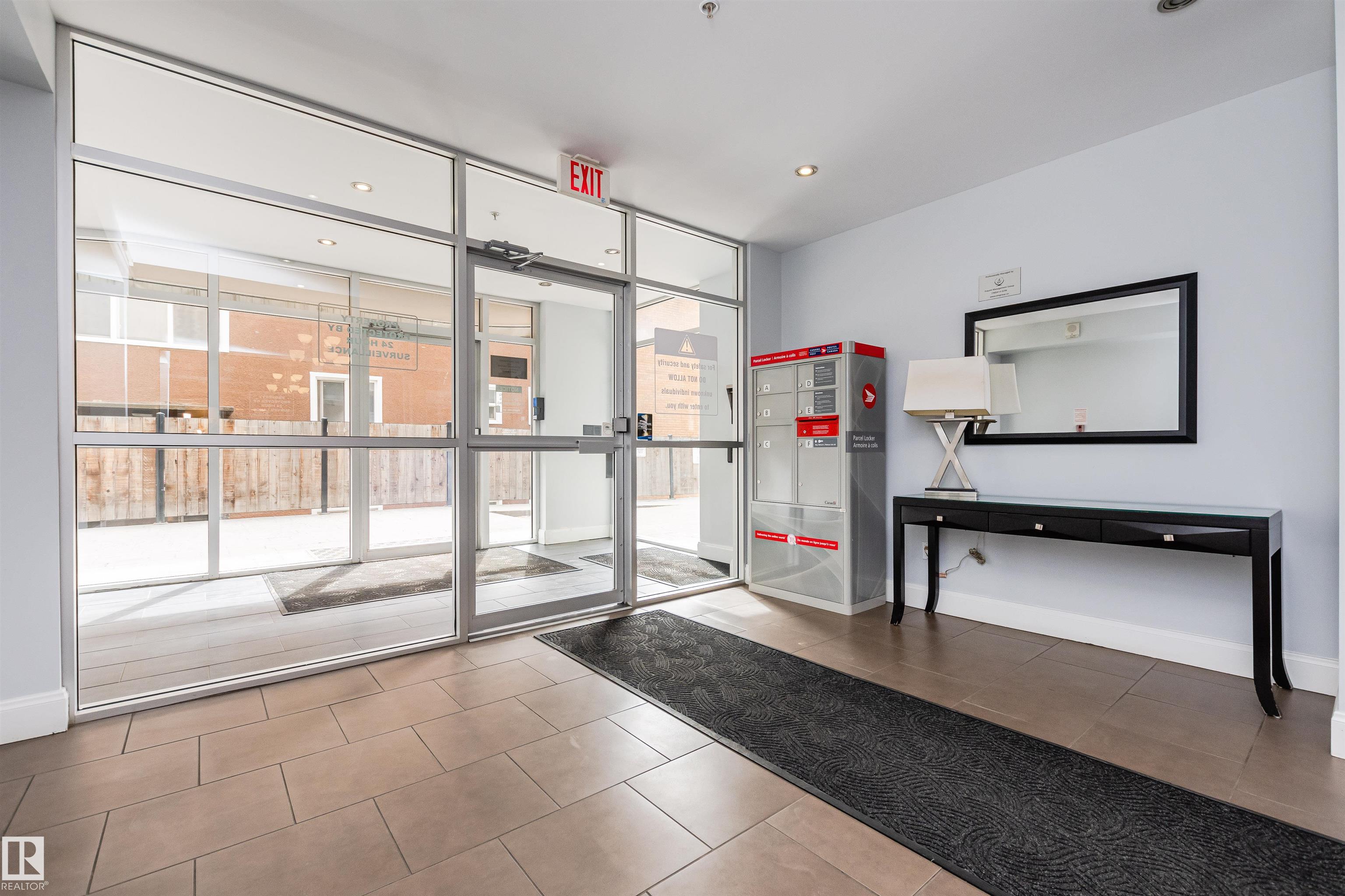 Condominium lobby with glass entry doors, parcel lockers, and a tiled floor.