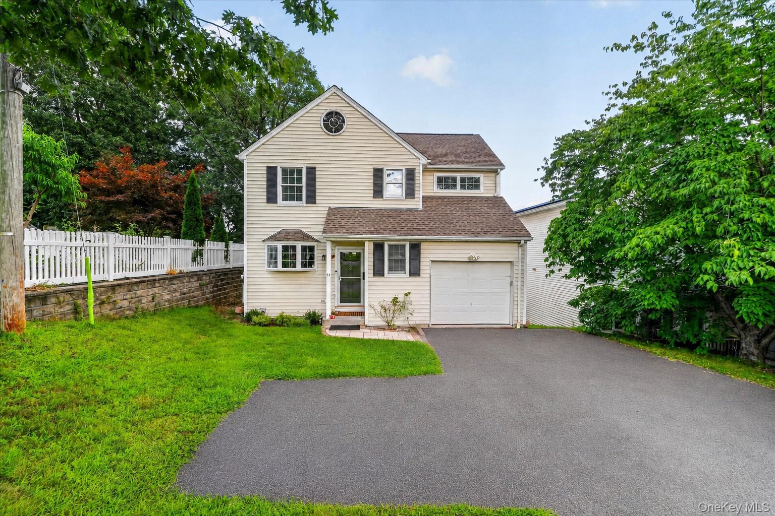 Beige two-story house with a single-car garage, broad driveway, and white picket fence.