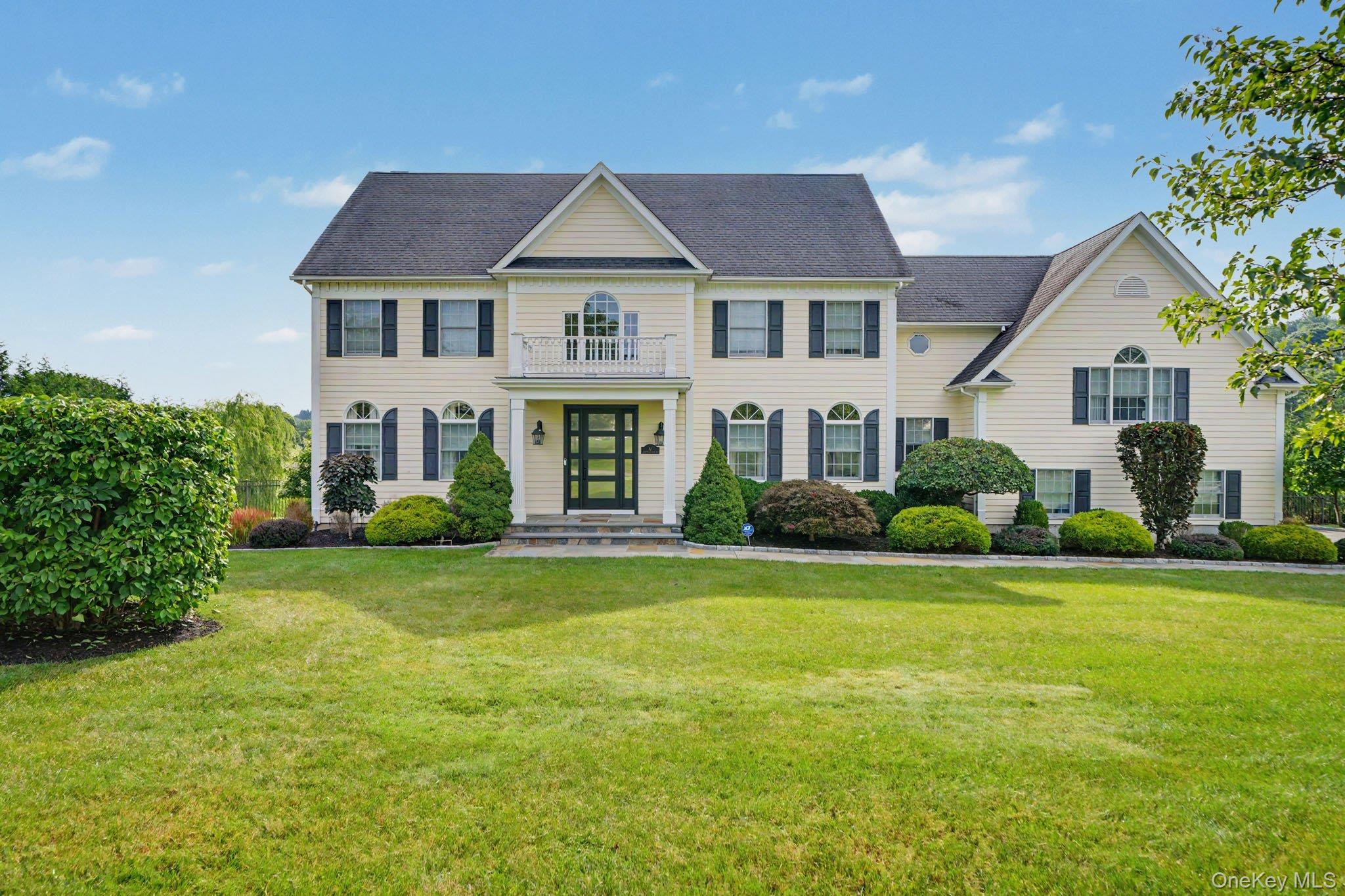 Cream two-story house with dark shutters, a central balcony, and a broad landscaped lawn.