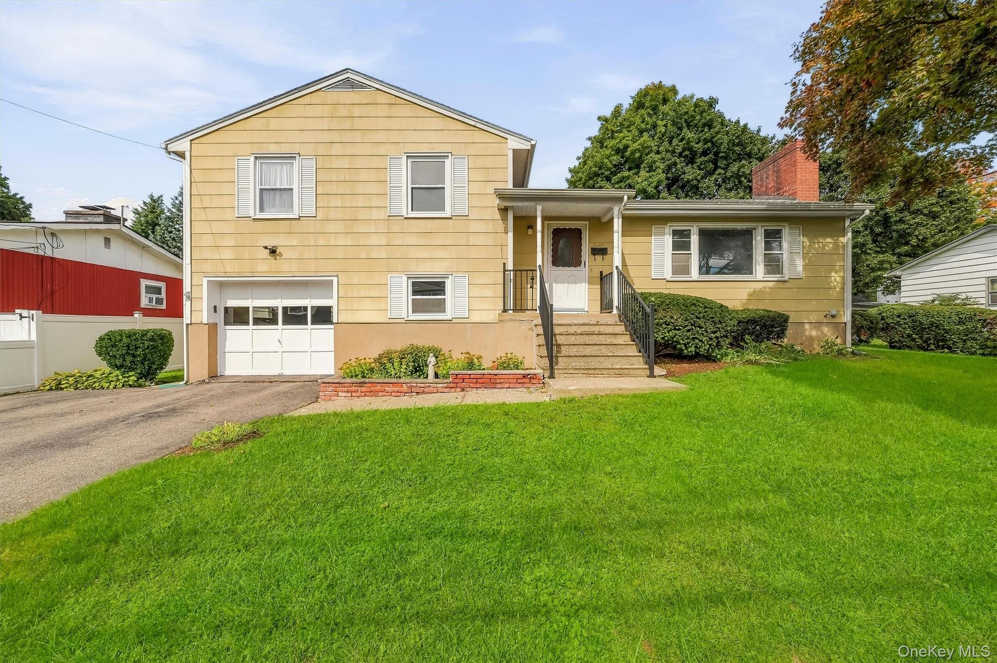 Yellow split-level home with attached garage, front steps, and broad green lawn.
