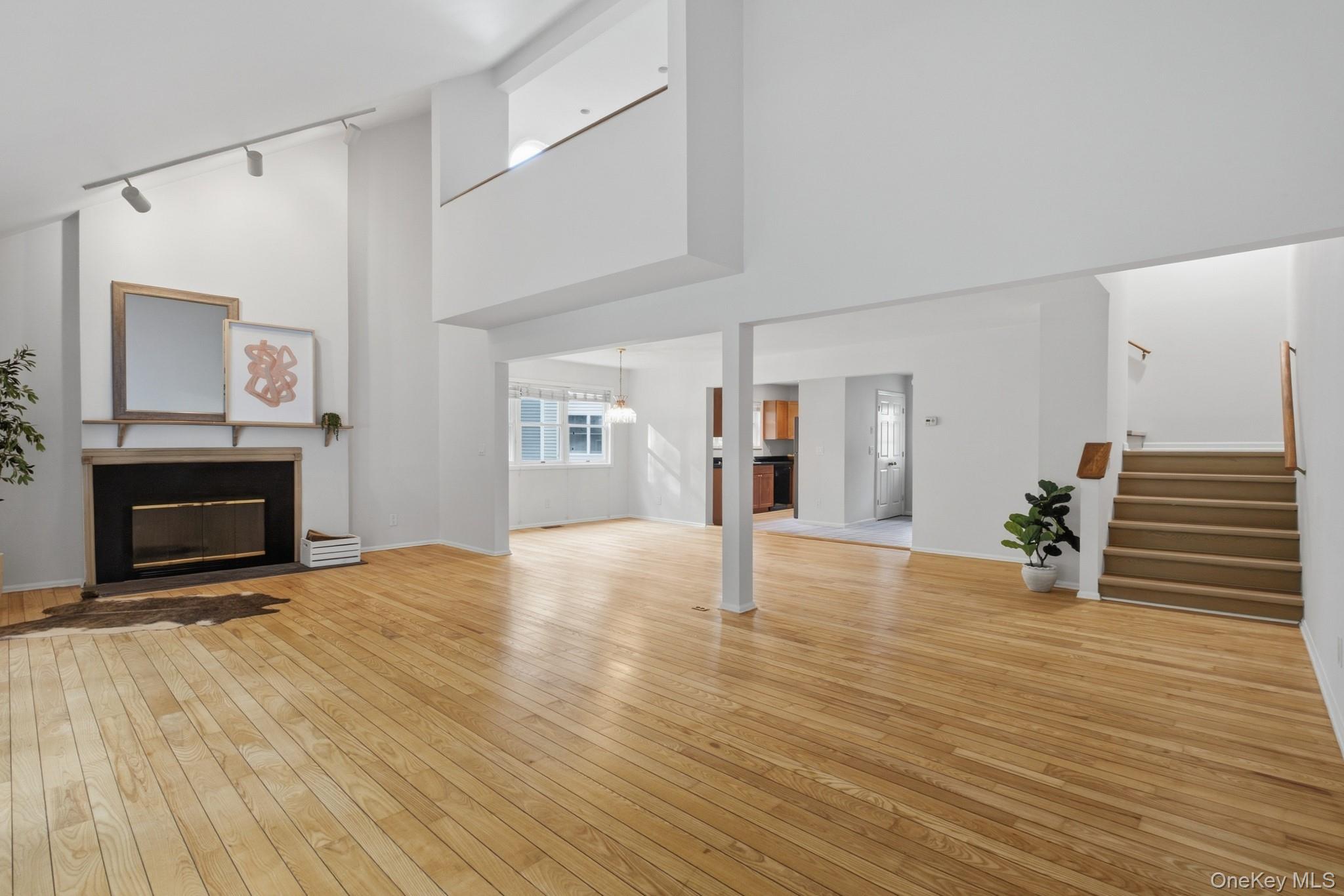 Open living room with polished hardwood floors, a fireplace, and stairs to the upper level.