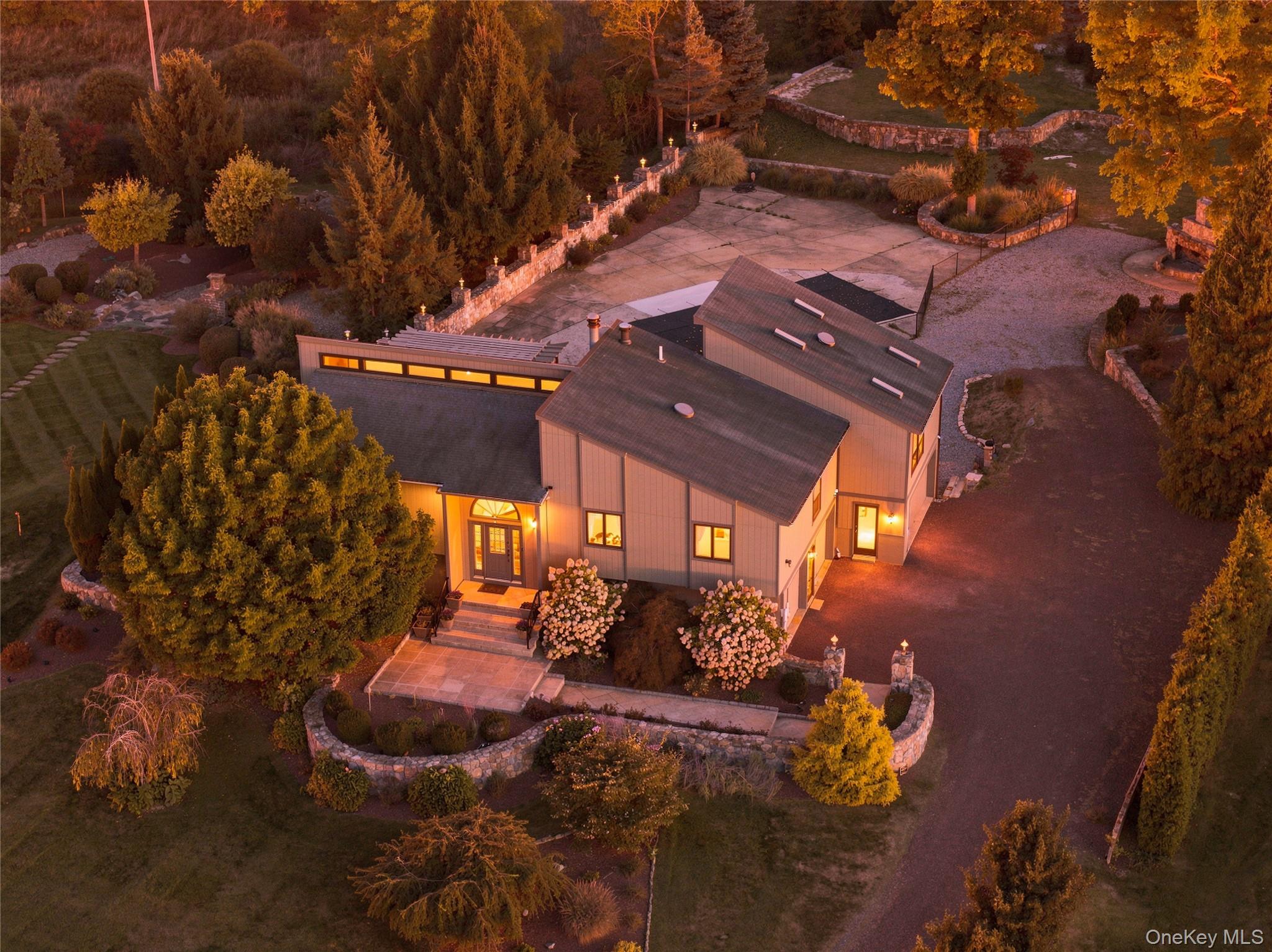 Aerial view of a modern home at dusk, with a stone-walled courtyard and autumn trees.