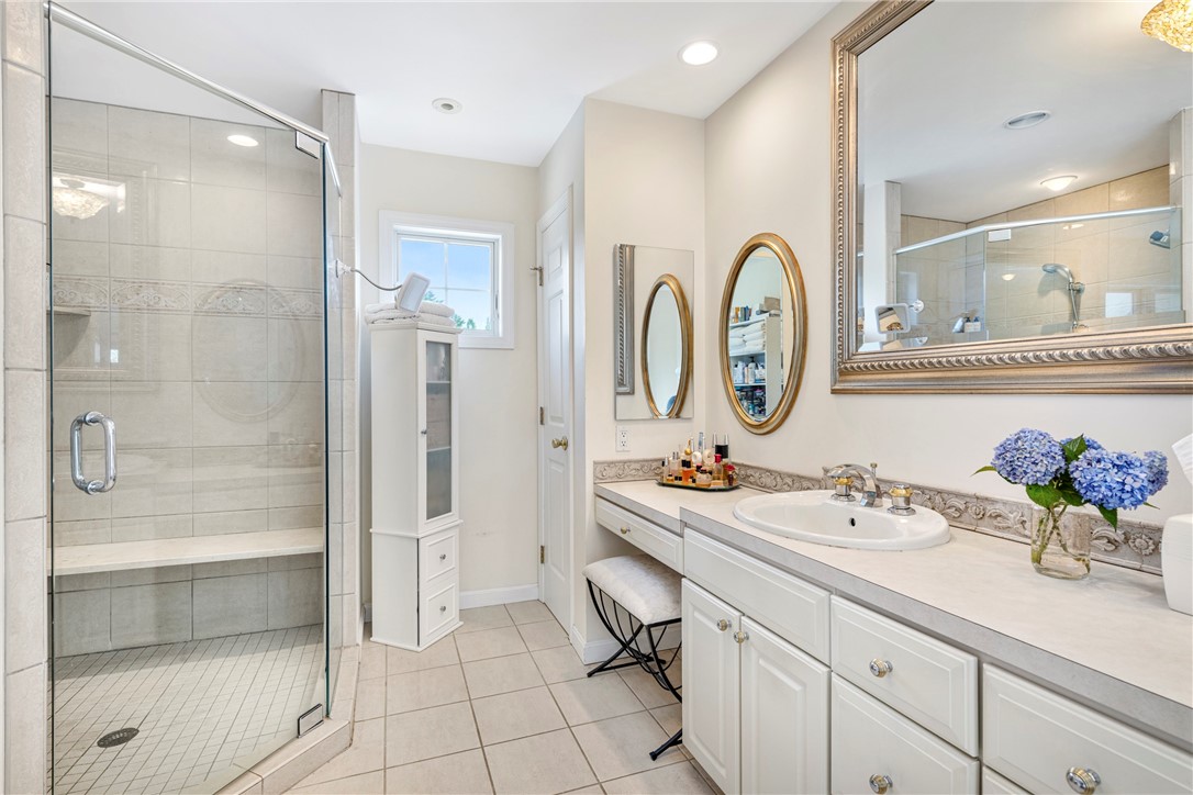 Bathroom with a glass-enclosed tiled shower, white vanity, and blue hydrangeas.
