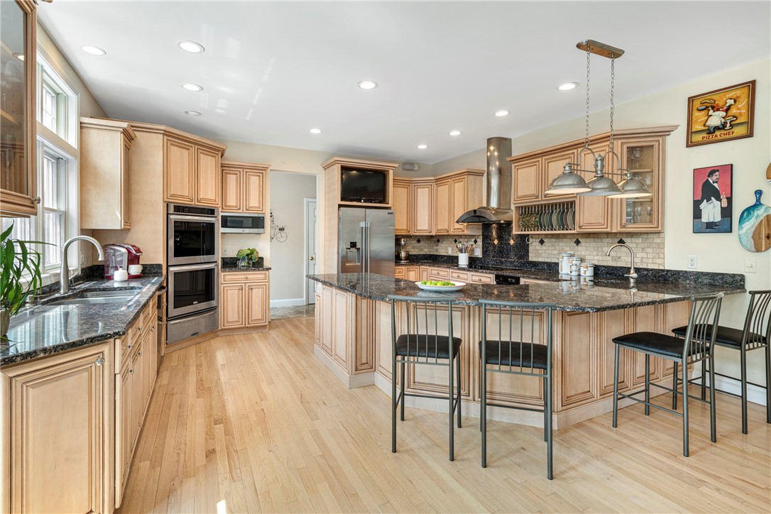 Kitchen with light wood cabinets, black granite counters, stainless steel appliances, and a large island with bar seating.
