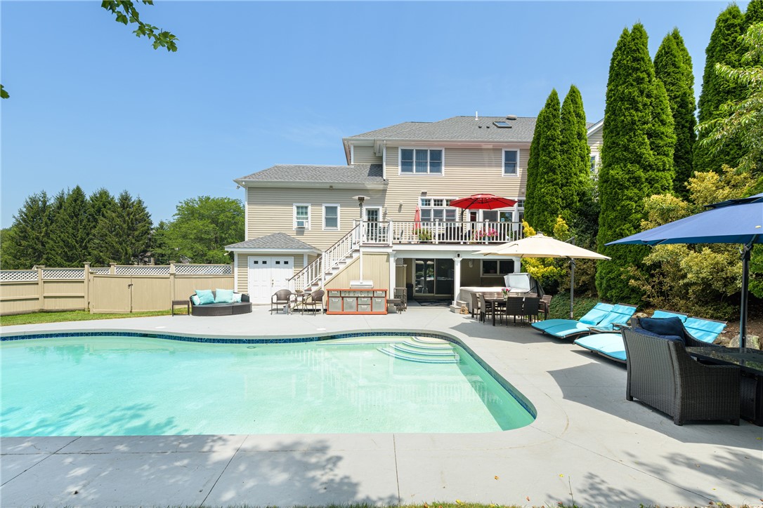Backyard swimming pool beside a beige two-story home, with a spacious patio and outdoor seating.