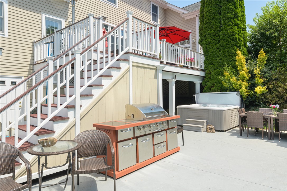 Outdoor patio with a large grill and hot tub beneath white-railed deck stairs.