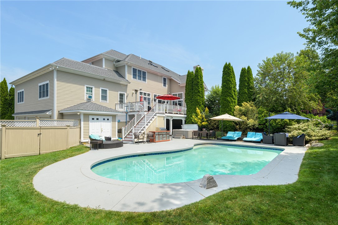 Home’s rear exterior with a raised deck and curved swimming pool in a landscaped backyard.