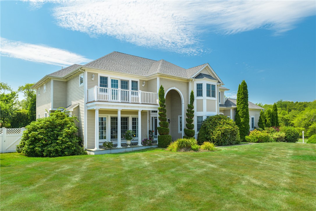 Two-story beige home with a white balcony, arched entry, and landscaped lawn.