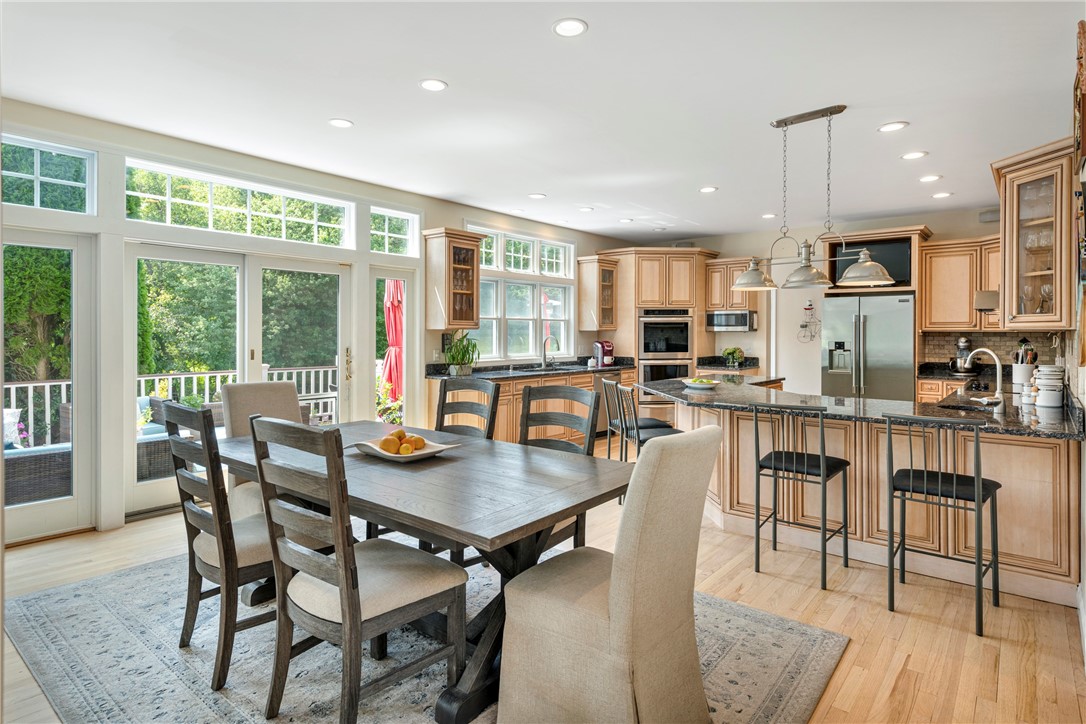 Kitchen and dining area with wood cabinetry, island seating, and tall garden-facing windows.