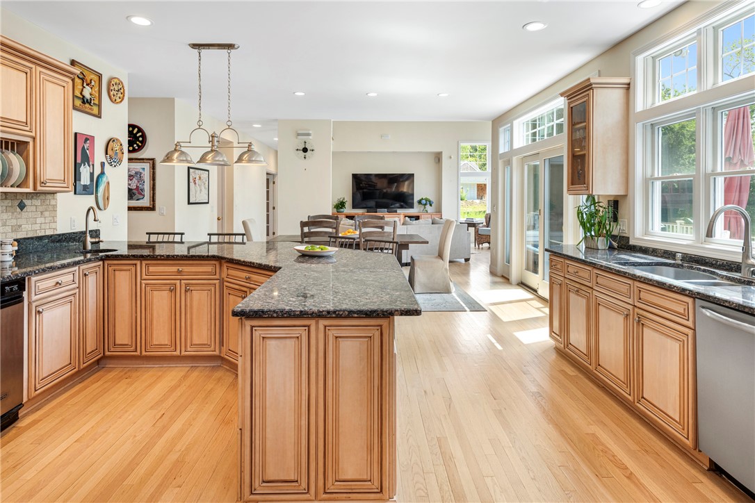Open-plan kitchen with a granite island, warm wood cabinets, and sunlit windows overlooking the living area.