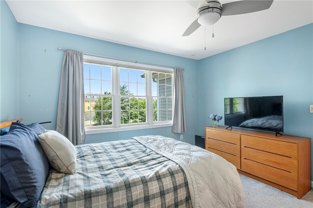 Bedroom with blue walls, plaid bedding, a large curtained window, and a wooden dresser with a television.