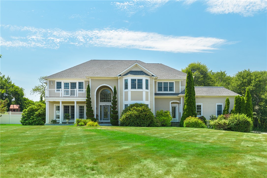 Two-story light-colored home with an arched entrance, second-floor balcony, and broad green lawn.
