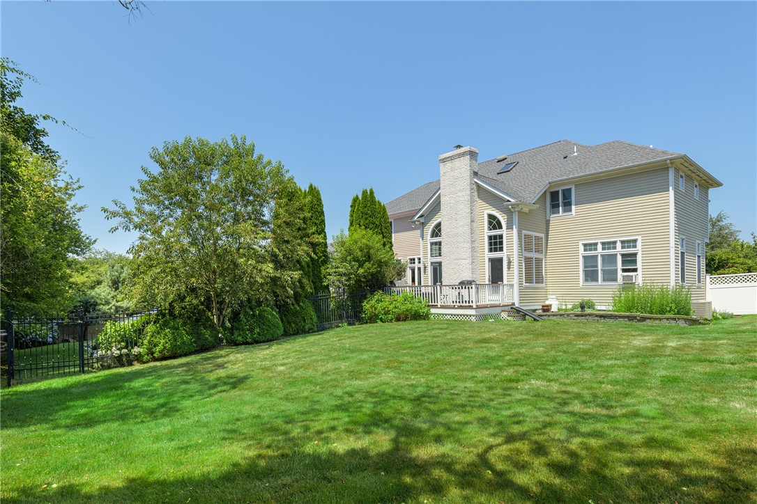 Rear of a beige two-story home with arched windows, a small deck, and a broad green lawn.