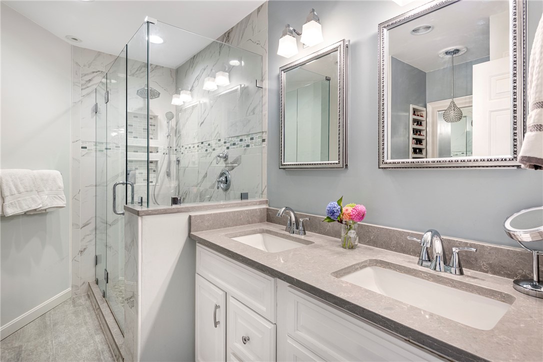 Bathroom with a glass-enclosed marble shower and gray stone double vanity.