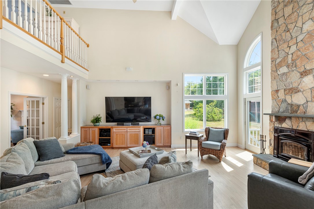 Living room with a vaulted ceiling, loft railing, tall windows, and stone fireplace.