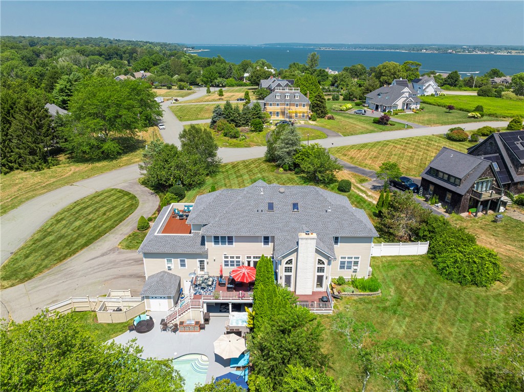 Aerial view of a coastal home with a pool, patio, and water beyond the neighborhood.