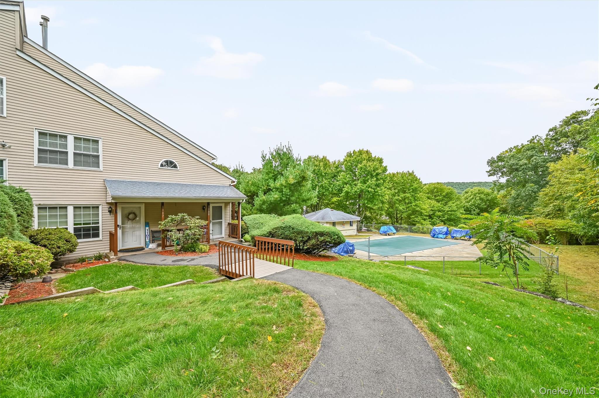Beige-sided home with a covered porch, curved walkway, and fenced outdoor court.