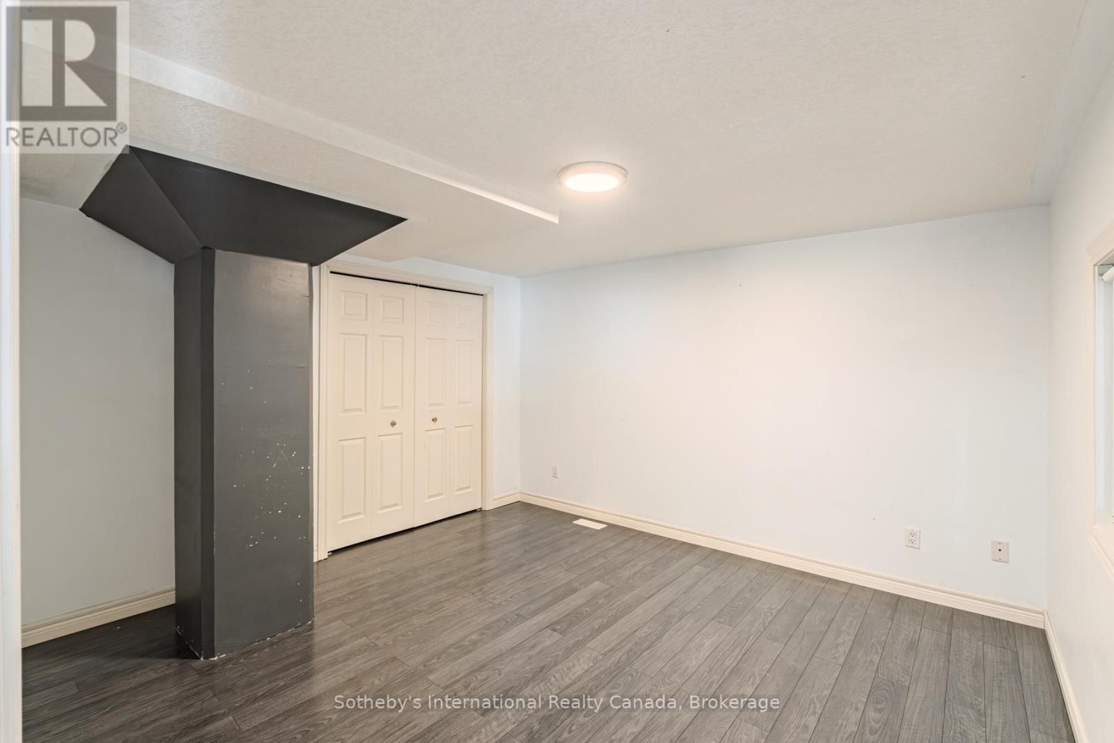 Empty room with gray plank flooring, a dark support column, and double closet doors.