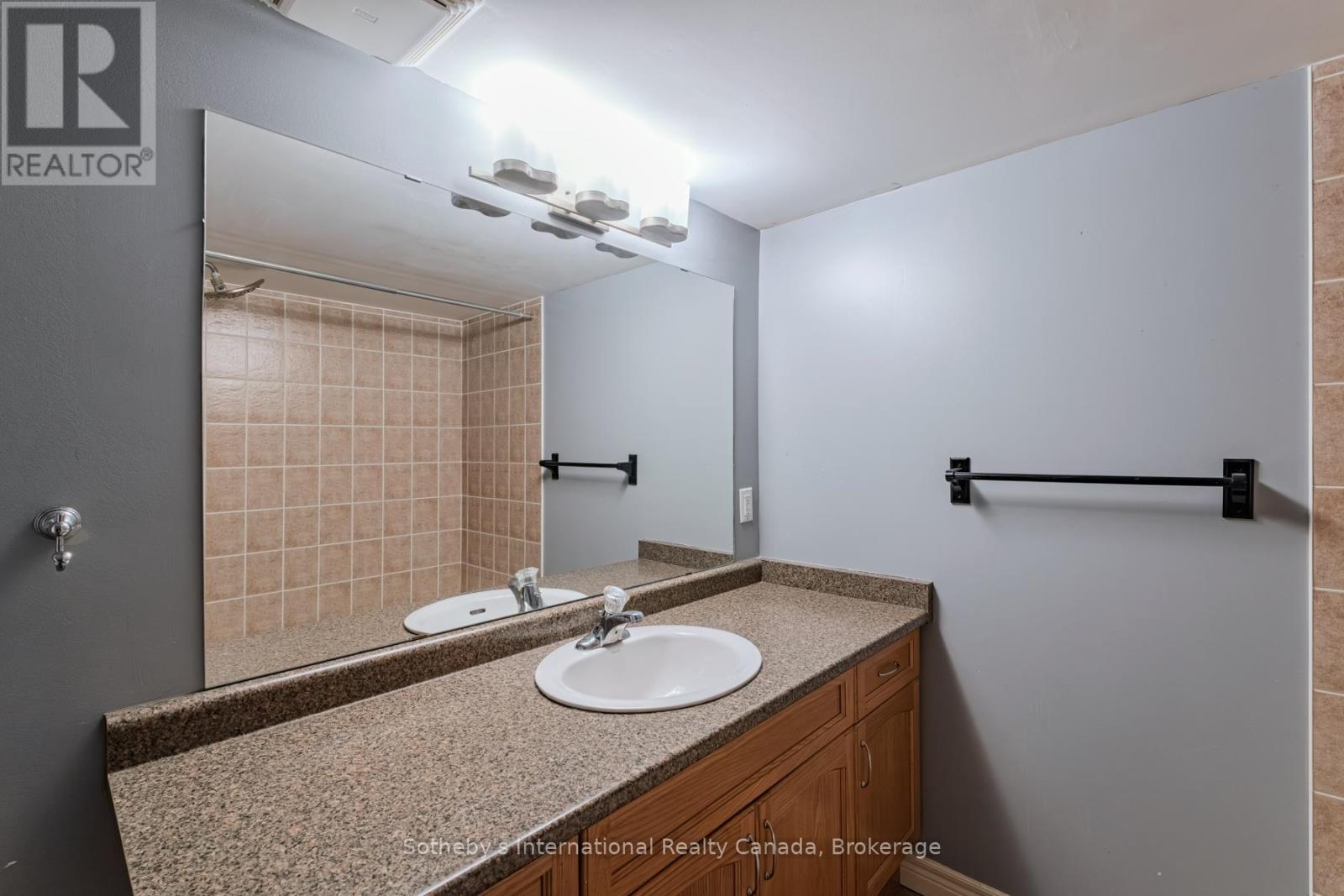 Bathroom vanity with a wide mirror, granite countertop, and wood cabinetry.