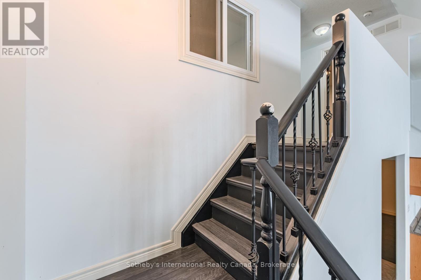 Interior staircase with dark wood treads, ornate black railing, and a high window.