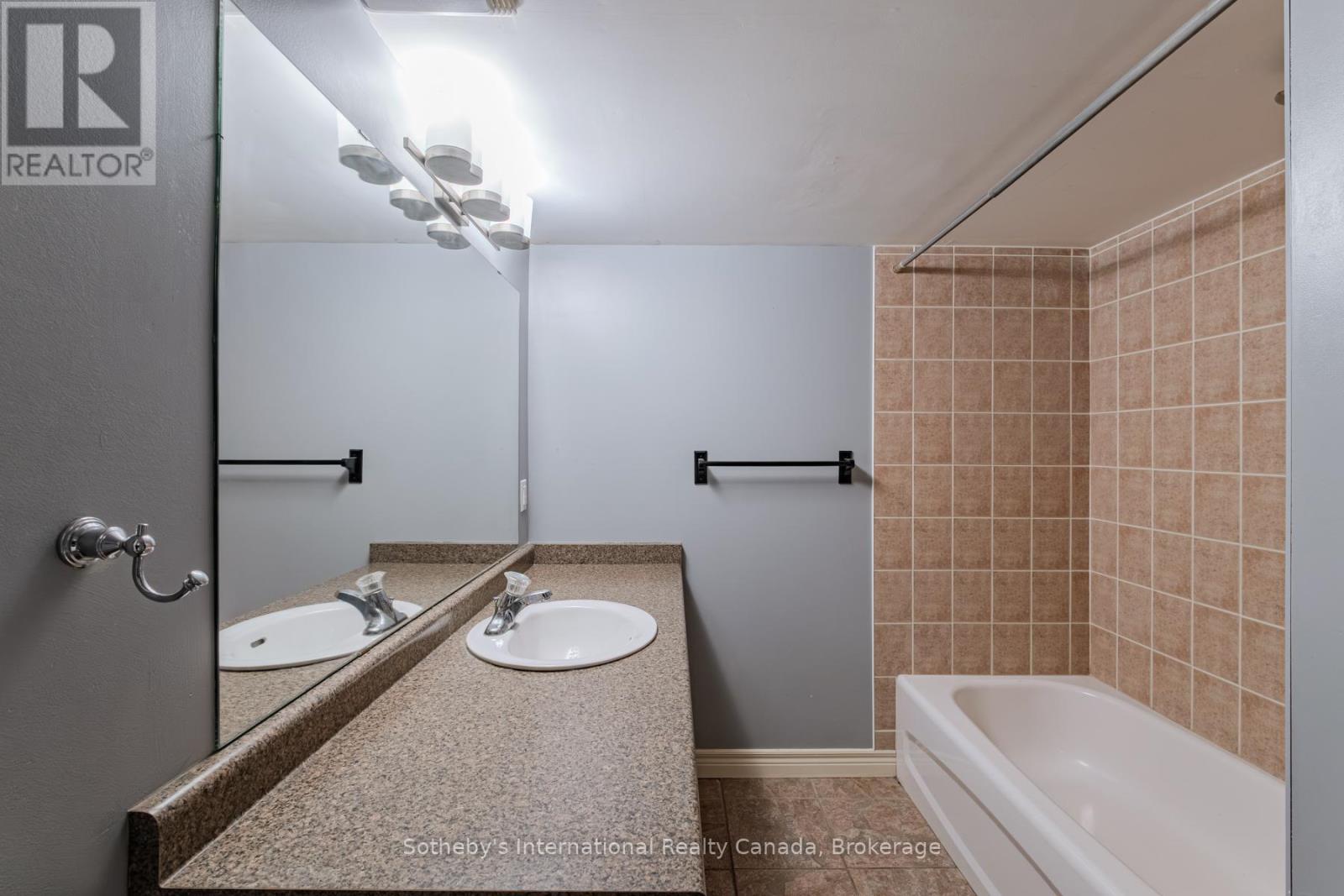 Bathroom with a granite-look vanity, large mirror, and tub beside tan tiled walls.