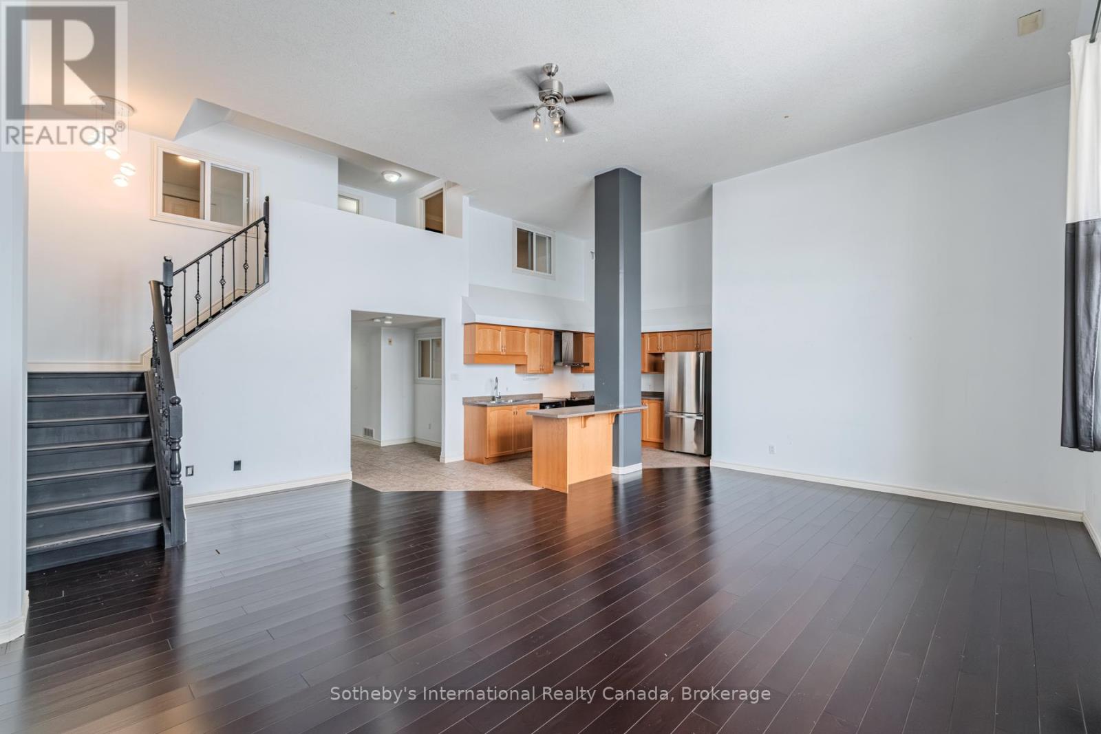 Living room with dark hardwood floors, a staircase, and an open kitchen with a breakfast bar.