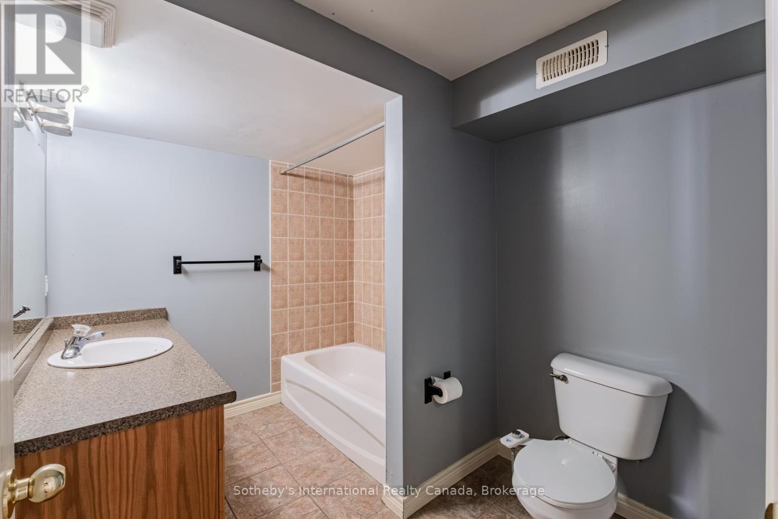 Bathroom with a wood vanity, bathtub with tiled surround, and separate toilet area.