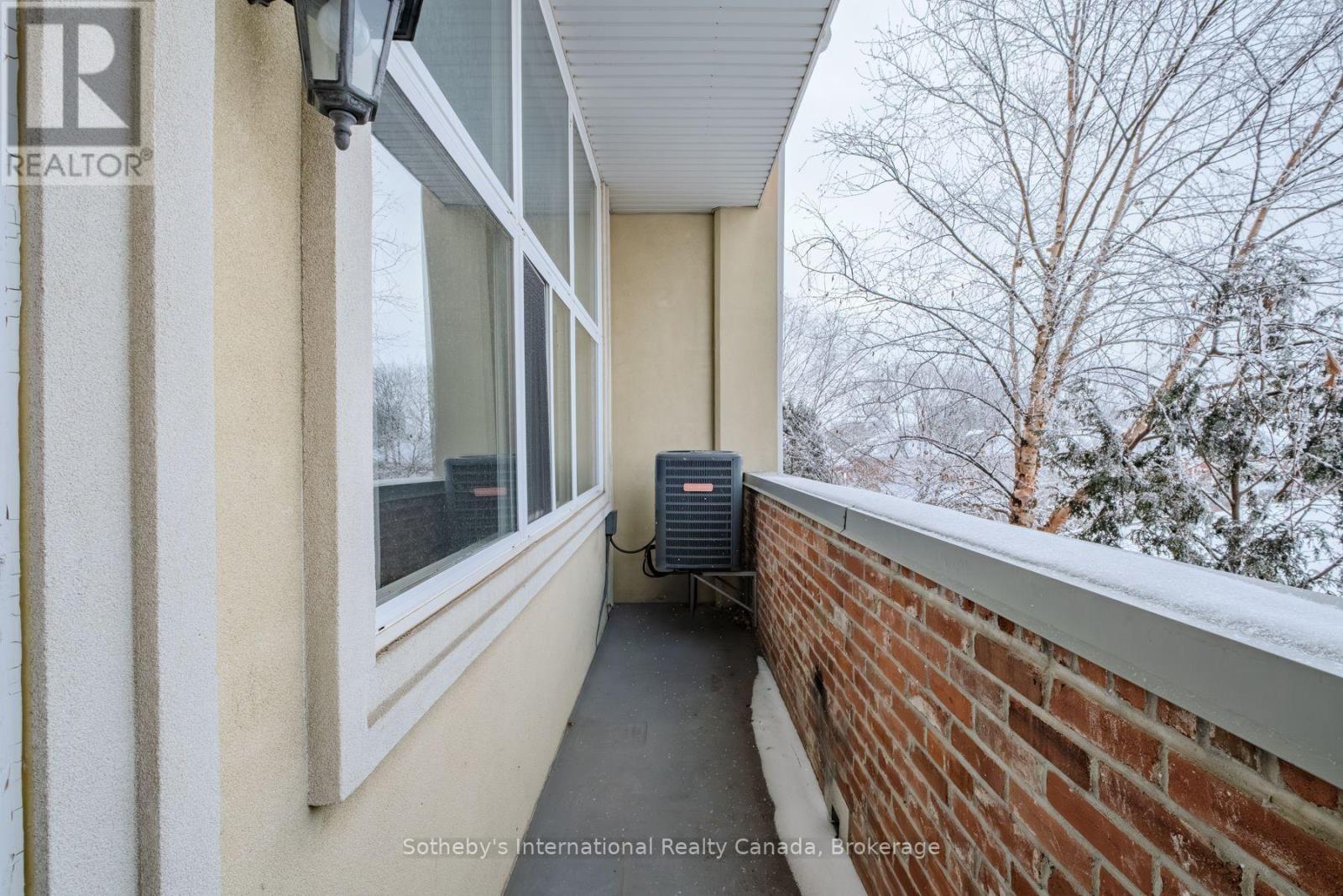 Narrow balcony with a brick railing, snow-covered trees, and an outdoor air-conditioning unit.