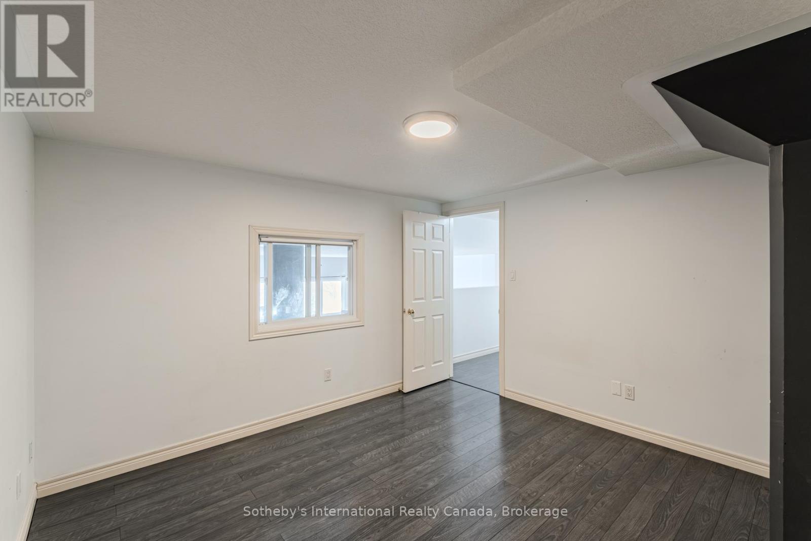 Vacant room with dark wood-look flooring, a small window, and an open doorway.