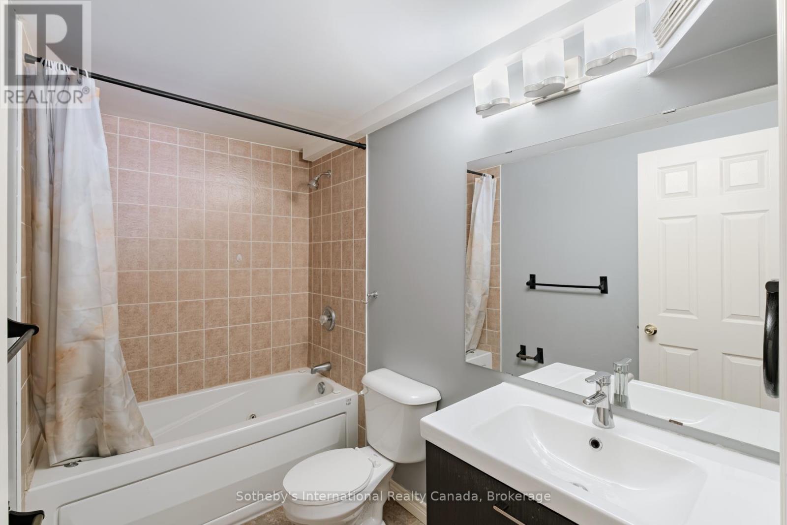 Bathroom with a tiled tub and shower, white vanity, large mirror, and toilet.