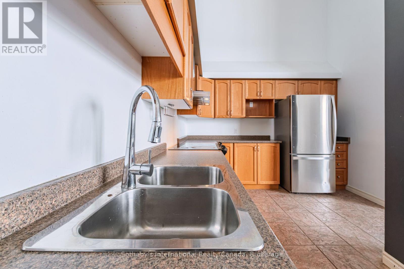 Kitchen with a double-basin sink, granite counters, maple cabinets, and stainless steel refrigerator.