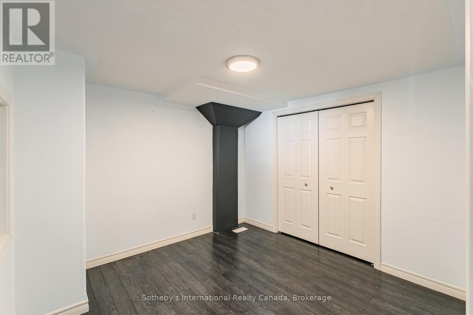 Empty room with dark flooring, white closet doors, and a black structural column.